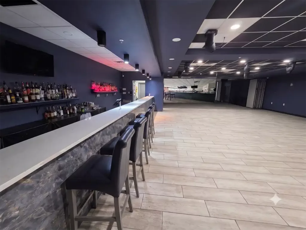 Empty modern nightclub interior featuring a long marbled bar counter with barstools and a spacious wooden dance floor.