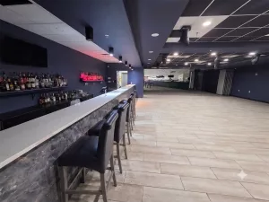 Empty modern nightclub interior featuring a long marbled bar counter with barstools and a spacious wooden dance floor.